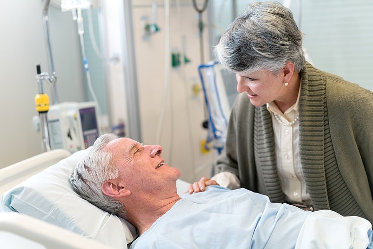 Patient wird am Bett von seiner Frau besucht