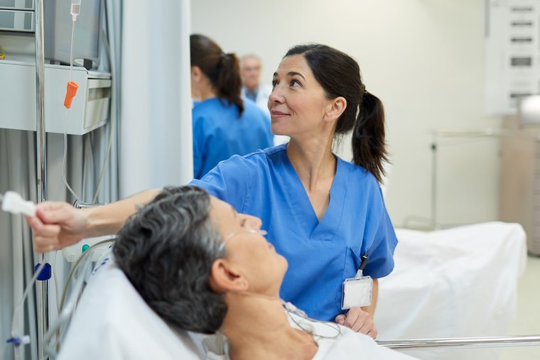 Foto Pflegekraft sitzt am Bett einer Patientin und überprüft die Schläuche einer Lösung
